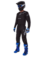 Motocross rider wearing complete Alpinestars racing gear, 2025 Racer Graphite Pants in Black and Gray, matching black jersey with grey logos, black helmet with blue goggles, bright blue and purple boots, and blue and grey gloves, coordinated outfit for off-road racing