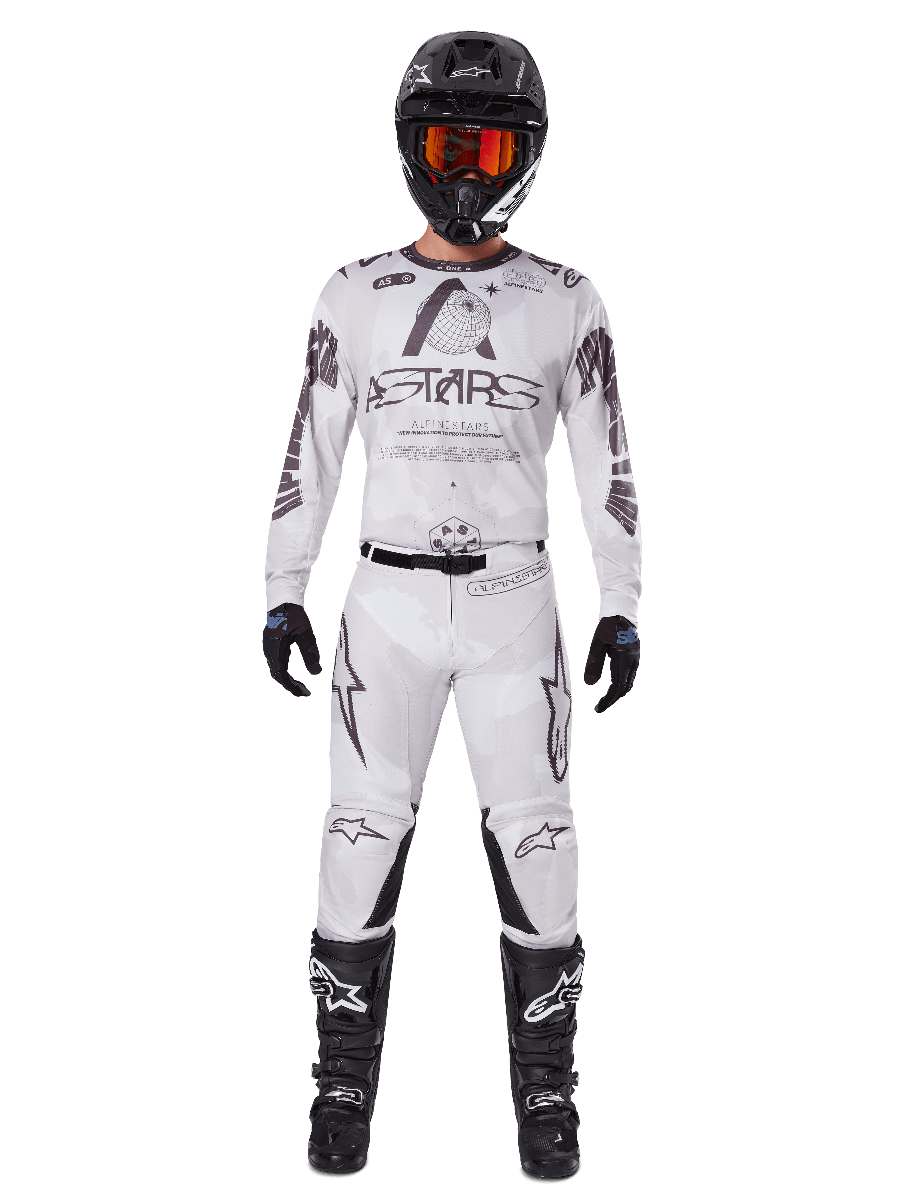 Pilote de motocross portant le pantalon Alpinestars 2025 Racer Hollow en Light Camo Brown, associé à un maillot à manches longues assorti blanc et gris, un casque noir avec lunettes orange-rouge, des gants noirs et des bottes noires, ensemble de course coordonné pour la performance tout-terrain.