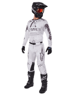 Alpinestars 2025 Racer Hollow Pants, pantalon de motocross, Brun Camo Clair, présenté dans un kit de course complet avec maillot blanc, casque noir et bottes noires, doté de panneaux de genoux noirs renforcés et d'un motif camouflage subtil.