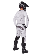 Alpinestars 2025 Racer Hollow Pants, pantalon de motocross, brun camouflage clair et blanc, vue arrière montrant un marquage noir imposant sur l'assise et des logos étoiles, porté avec un maillot assorti, des bottes noires et un casque noir pour un look de course tout-terrain complet