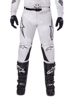 Pantalon Alpinestars 2025 Racer Hollow, pantalon de motocross, camouflage brun clair, porté avec des gants noirs et des bottes de motocross, doté d'un motif camouflage subtil avec des graphismes noirs et les logos Astars, conception ergonomique pour une conduite tout-terrain performante