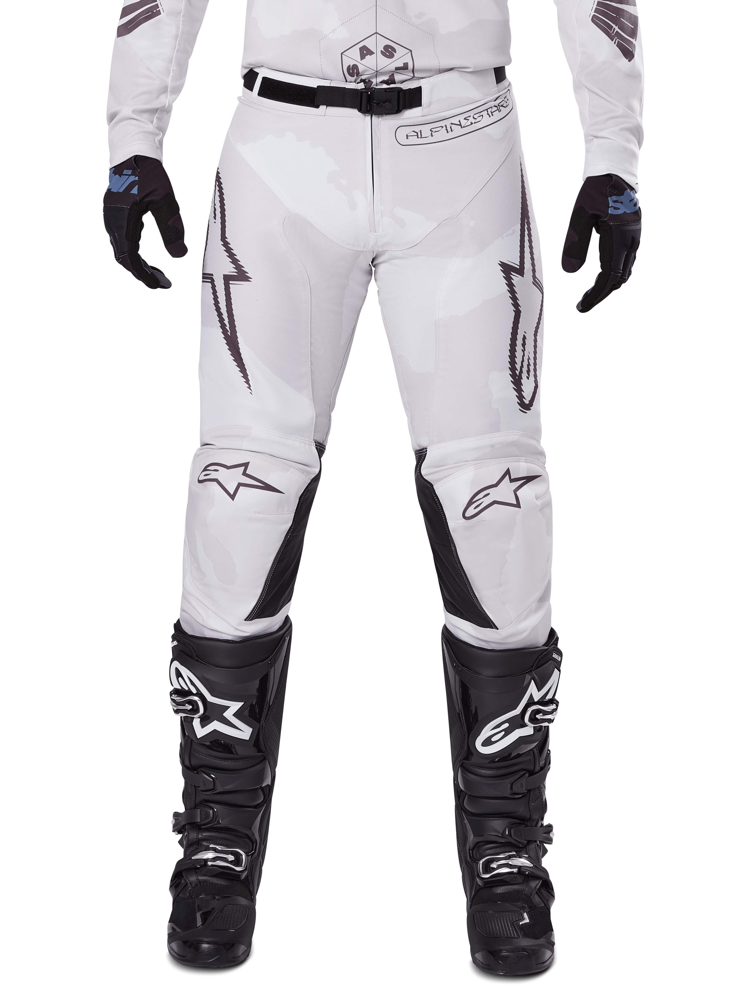 Pantalon Alpinestars 2025 Racer Hollow, pantalon de motocross, camouflage brun clair, porté avec des gants noirs et des bottes de motocross, doté d'un motif camouflage subtil avec des graphismes noirs et les logos Astars, conception ergonomique pour une conduite tout-terrain performante