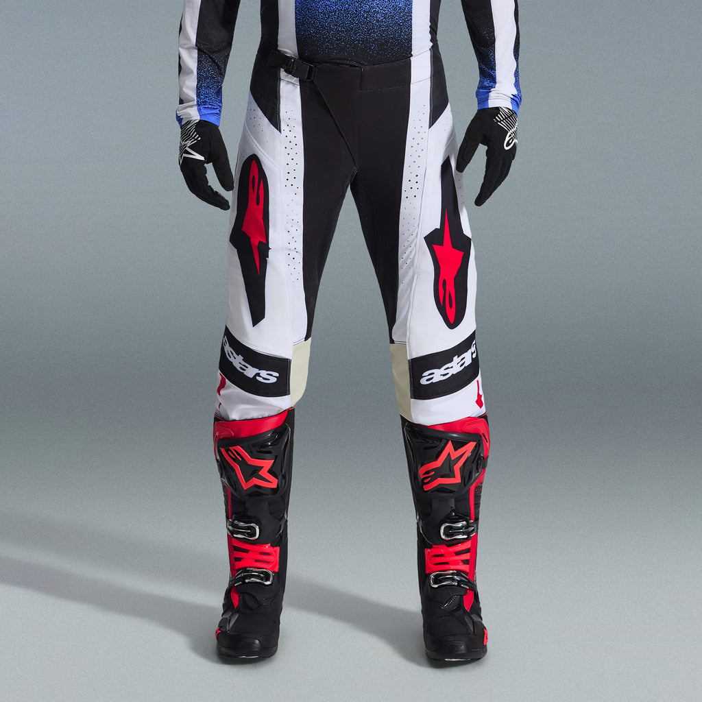 Ensemble d'équipement Alpinestars Techstar Knif 2026, équipement de motocross, pantalon noir et blanc avec de grands logos étoile rouges, porté avec des bottes de course noires et rouges et des gants noirs, coupe athlétique professionnelle pour la performance tout-terrain