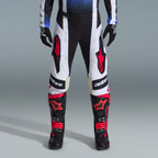 Ensemble d'équipement Alpinestars Techstar Knif 2026, équipement de motocross, pantalon noir et blanc avec de grands logos étoile rouges, porté avec des bottes de course noires et rouges et des gants noirs, coupe athlétique professionnelle pour la performance tout-terrain