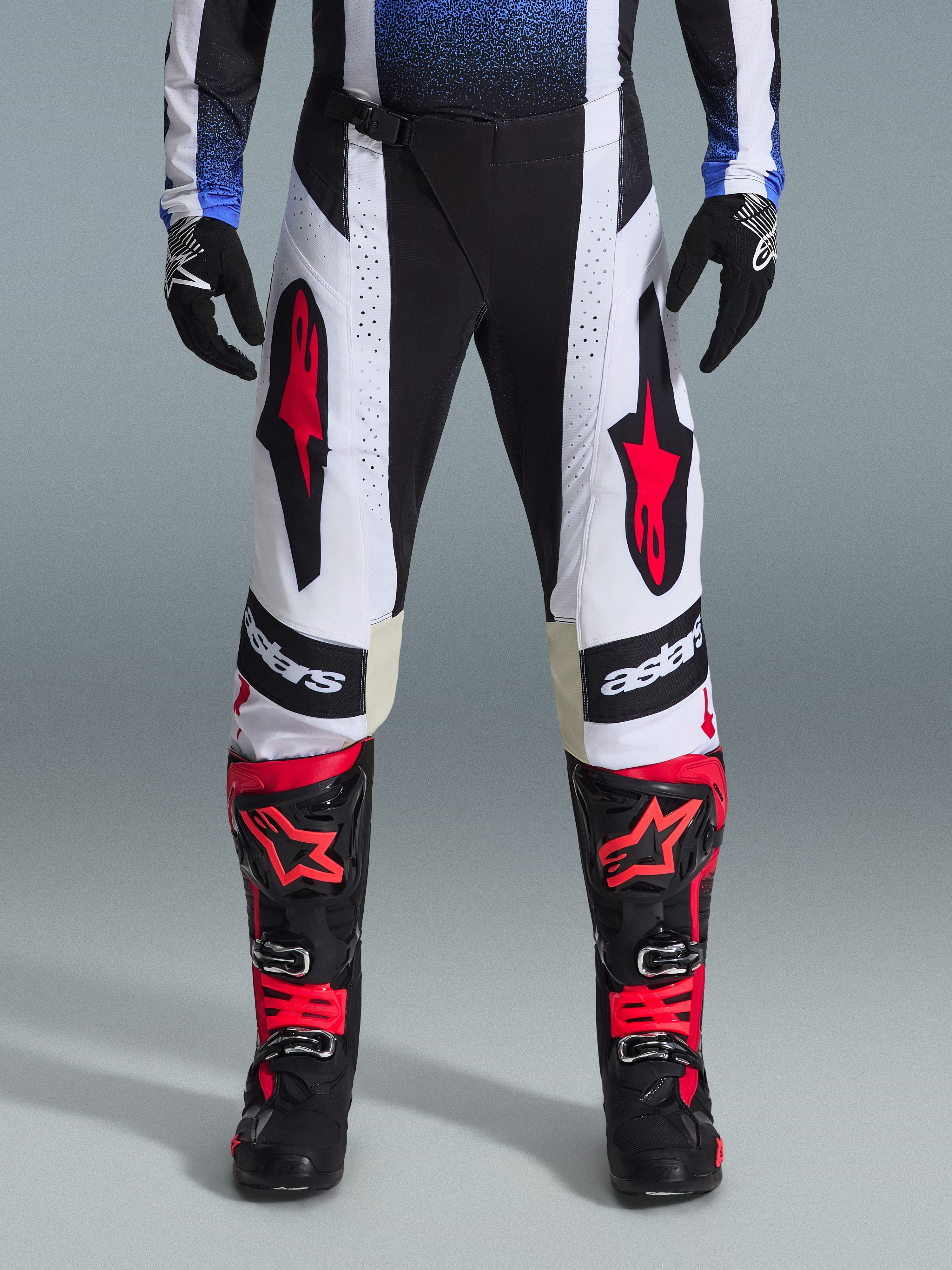 Pantalon Alpinestars Techstar Knif 2026, pantalon de motocross, noir, blanc et rouge, porté avec des bottes rouges et noires assorties et des gants noirs, avec des logos d'étoiles rouges proéminents sur des panneaux blancs et des détails techniques perforés pour la course tout-terrain.
