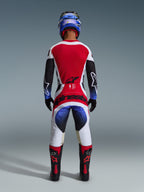 Alpinestars 2026 Techstar Knif Pants, Motocross Pants, Black White Red and Blue, back view of a rider in complete gear including matching jersey, blue helmet, and black and red boots, featuring bold Alpinestars branding on the seat.