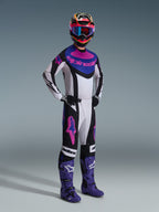 Motocross rider wearing the Alpinestars 2026 Techstar Knif Gear Set, Black Light Gray and Purple, white jersey with blue and pink accents, matching pants with purple star logos, colorful pink and yellow helmet, purple motocross boots, and black gloves, professional gear set for off-road racing.