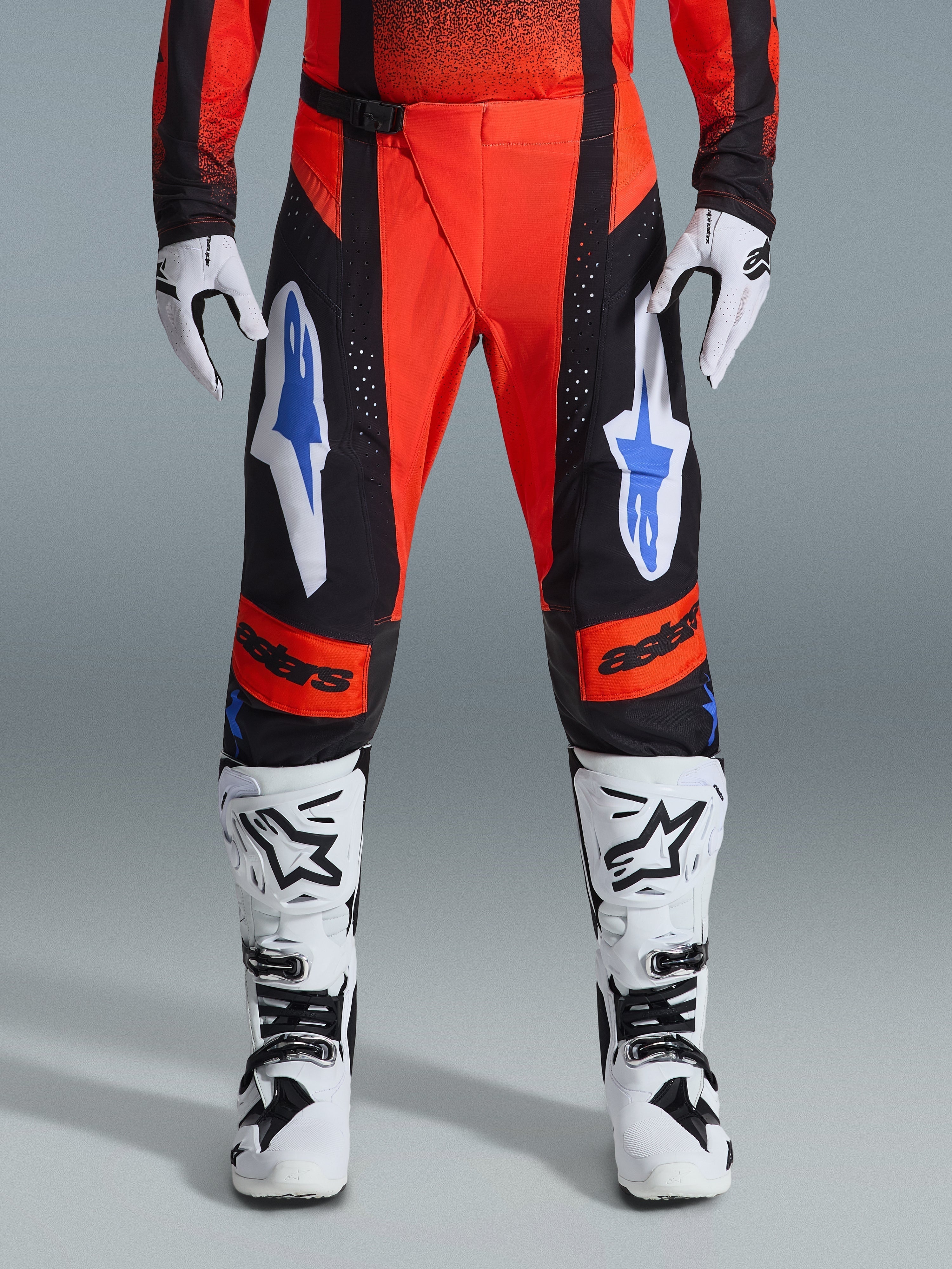 Alpinestars 2026 Techstar Knif Pants, pantalon de motocross, orange, noir et bleu UCLA, porté avec le maillot assorti, des bottes de motocross blanches et noires et des gants, arborant un logo audacieux sur les cuisses et les genoux, coupe athlétique pour la course tout-terrain