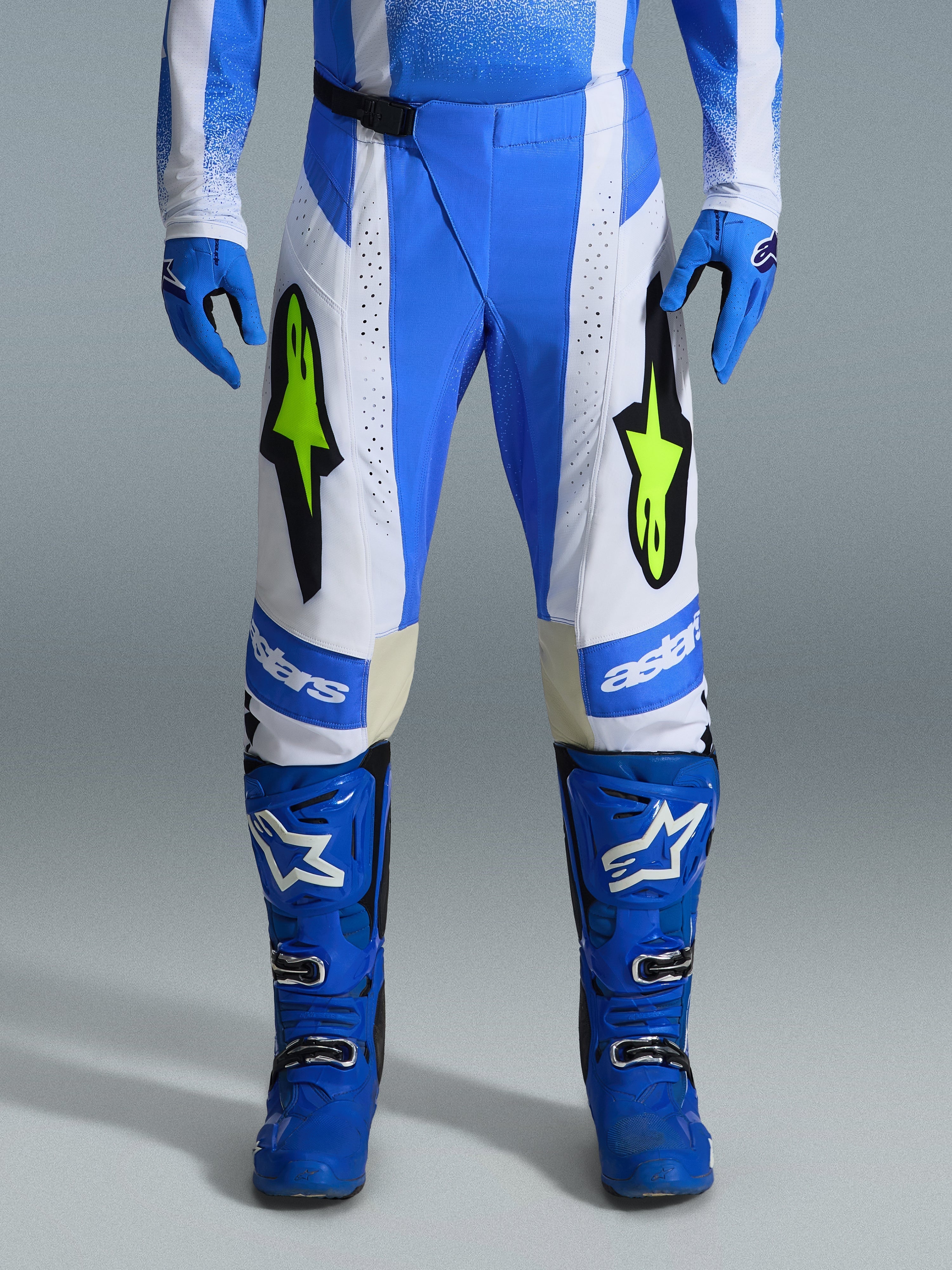 Alpinestars 2026 Techstar Knif Pants, pantalon de motocross, bleu UCLA, noir et jaune fluo, porté avec des gants et des bottes bleus assortis, doté de panneaux blancs et de logos jaune fluo éclatants, coupe de course ergonomique pour la performance tout-terrain