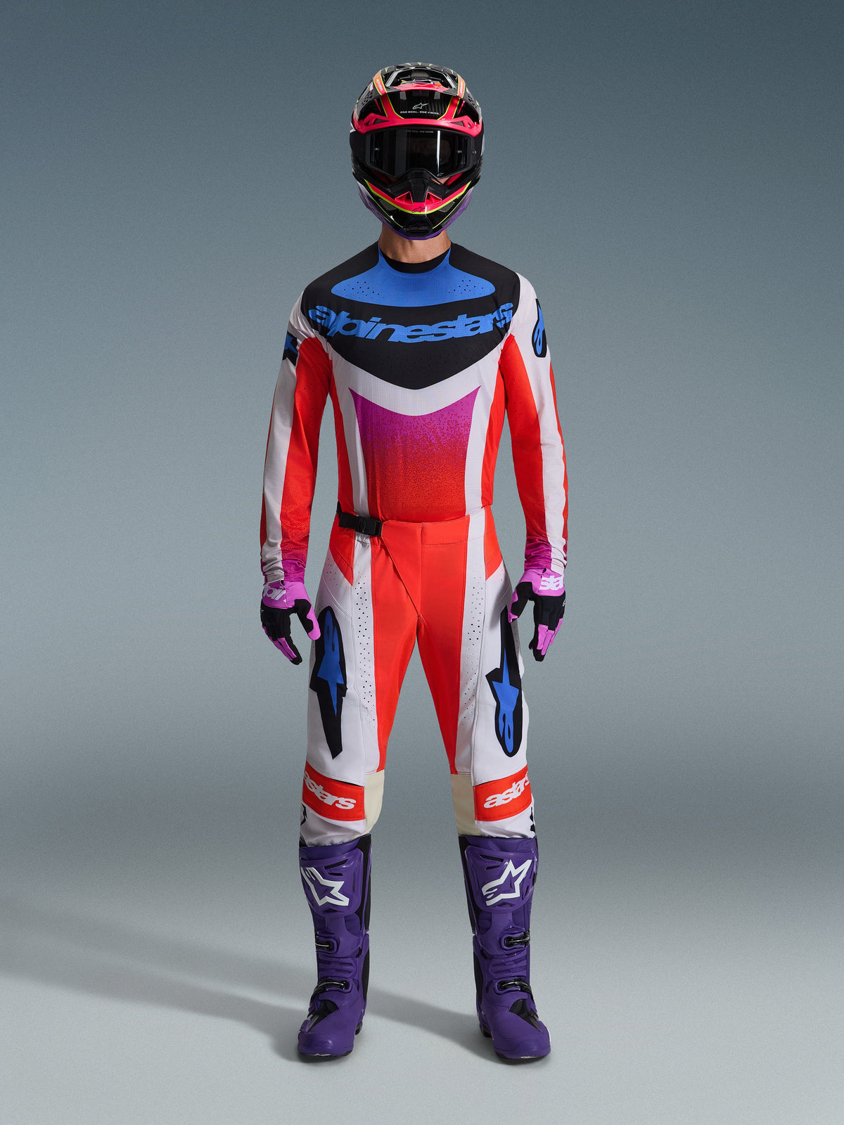 Motocross rider wearing the 2026 Techstar Knif Gear Set, complete racing outfit in red, white, and black with blue branding and pink accents, featuring purple boots with white logos, pink and black gloves, and a black and pink helmet, professional off-road racing gear