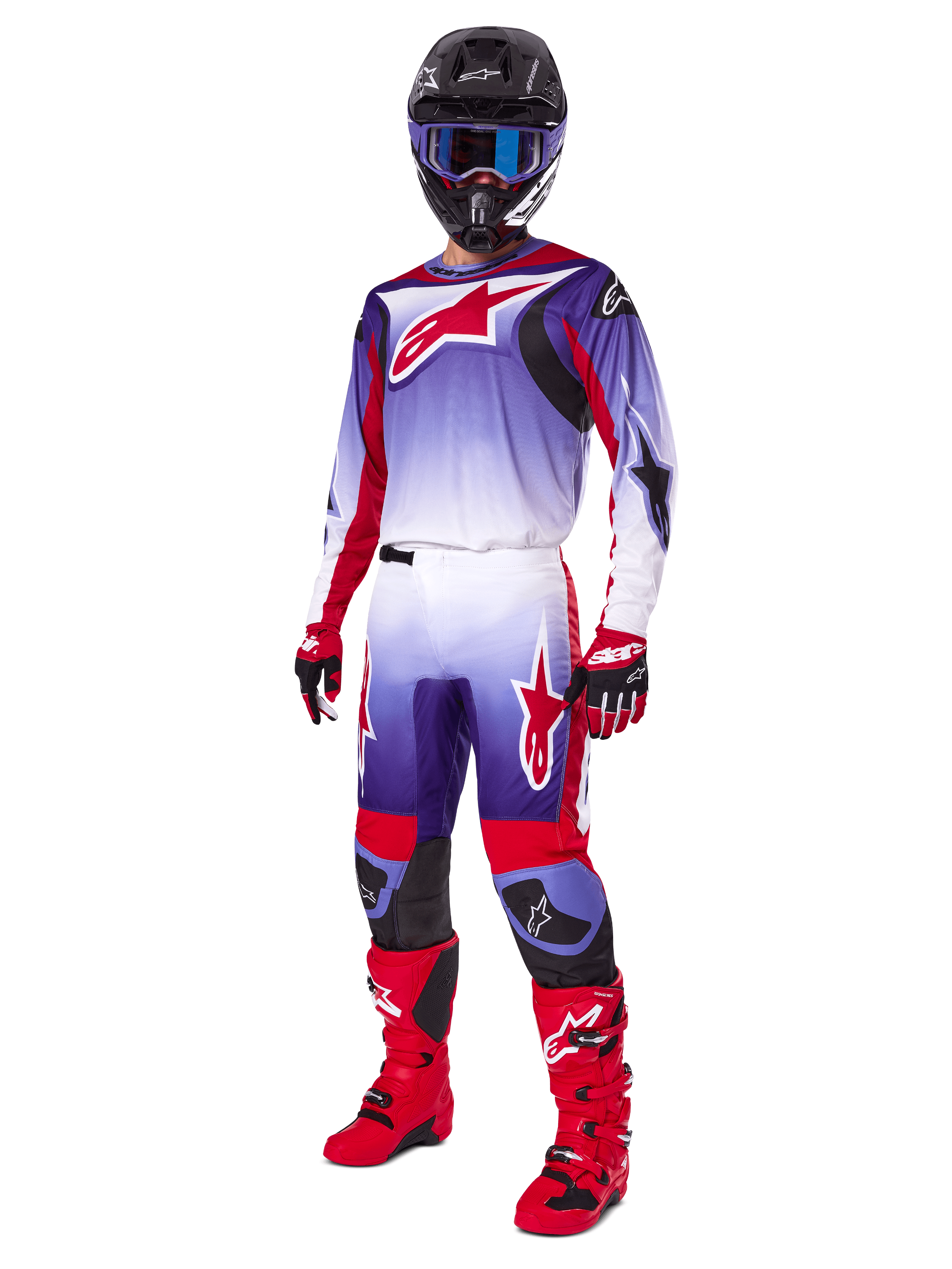 Pilote de motocross portant une tenue de course complète, pantalon Fluid Wurx 2025 et maillot assorti en violet, rouge vif et blanc, grand logo Alpinestars rouge, bottes et gants rouges, casque noir avec lunettes bleues, tenue coordonnée pour la course tout-terrain
