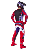 Pilote de motocross de dos portant le pantalon Alpinestars Fluid Wurx 2025, pourpre et rouge vif avec des accents blancs et noirs, maillot assorti, casque noir et bottes rouges, tenue coordonnée pour la course tout-terrain