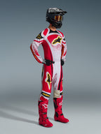 Alpinestars 2026 Techstar Nomur Pants, Motocross Pants, Red and White with black and yellow accents, worn by a rider with a matching racing jersey, bright red boots, and a black helmet with gold goggles, complete professional off-road competition outfit