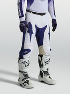 Alpinestars pantalon Racer Air Amber, pantalon de motocross pour homme, bleu et blanc, polyfibre perforée et coupe de course pré-courbée, porté avec des bottes de moto blanches.