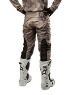 Alpinestars 2024 Racer Tactical Pants, pantalon de motocross, camouflage vert militaire et marron, vue arrière montrant le motif camouflage et les panneaux extensibles noirs respirants sur le bas des jambes, porté avec des bottes de motocross blanches, équipement technique durable pour la conduite tout-terrain