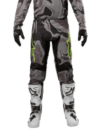 Pantalon Alpinestars Racer Tactical 2024, pantalon de motocross, Cast Gray Camo Magnet, porté avec un maillot camouflage assorti, des gants noirs et des bottes blanches et noires, avec des logos étoilés vert citron sur les cuisses et des empiècements stretch noirs, vue de face d'un équipement de pilotage tout-terrain.