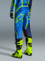Alpinestars 2026 Fluid Apex Pants, pantalon de motocross, bleu et jaune fluo, vue arrière d'un pilote portant une tenue assortie et des bottes jaune fluo, arborant des logos Alpinestars audacieux et un design ergonomique