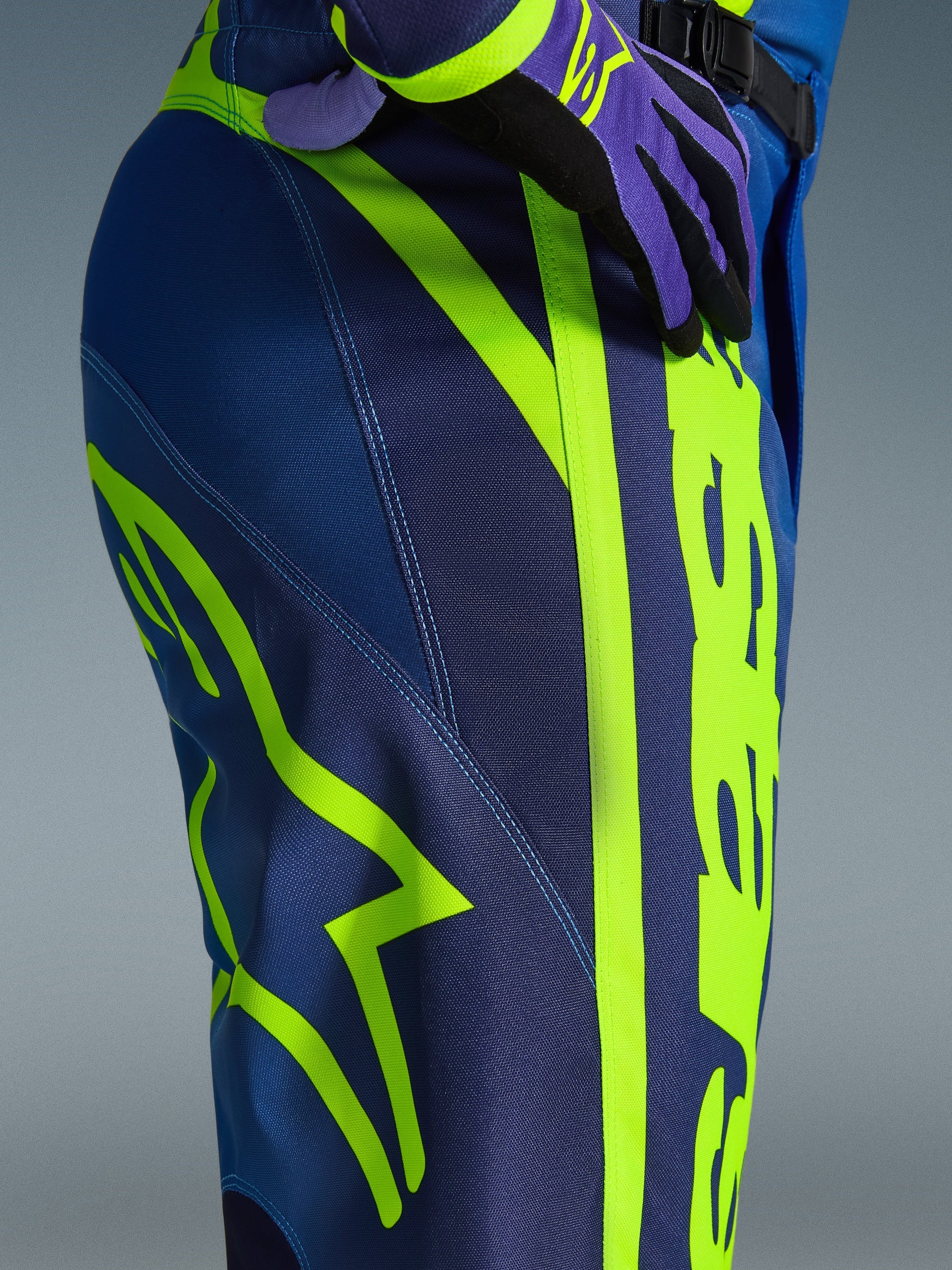 Alpinestars 2026 Fluid Apex Pants, pantalon de motocross, bleu et jaune fluo, vue rapprochée du côté et de la hanche avec marquage Alpinestars jaune fluo audacieux, matériau poly-tissu durable pour la conduite tout-terrain, fait partie d'un ensemble d'équipement assorti