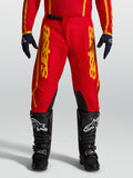 Alpinestars Pantalon Fluid Apex V2, pantalon de motocross pour homme, rouge et doré, construction robuste en poly-tissu 600D avec logos latéraux, porté avec des bottes de moto noires