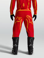 Alpinestars Pantalon Fluid Apex V2, pantalon de motocross pour homme, rouge et doré, vue de dos avec bottes noires.