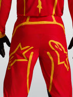 Alpinestars Fluid Apex V2, pantalon de motocross rouge et doré, empiècement arrière renforcé et motifs d'étoiles.