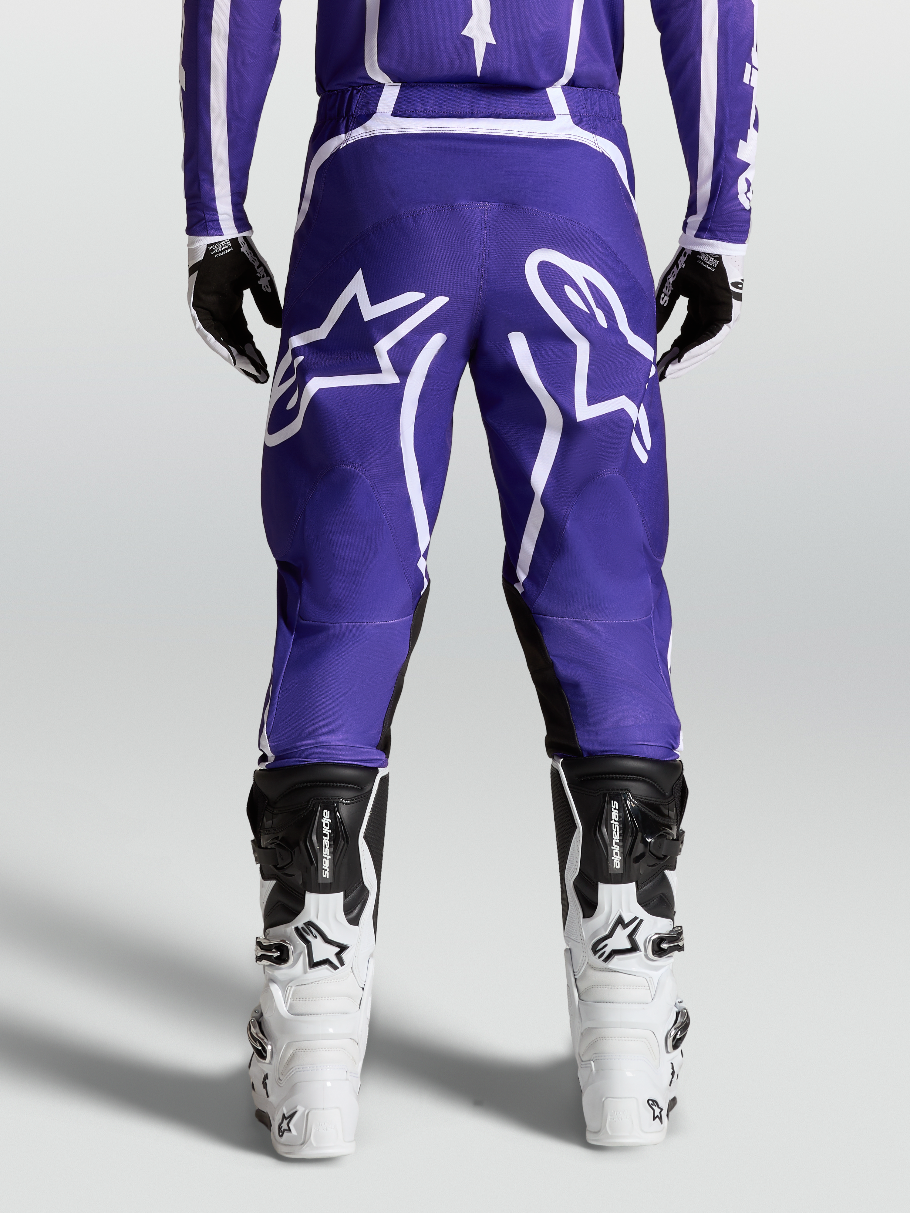 Alpinestars Pantalon Fluid Apex V2, pantalon de motocross tout-terrain, bleu et blanc, vue de dos sur mannequin avec bottes blanches, poly-tissu 600D durable et design ergonomique.
