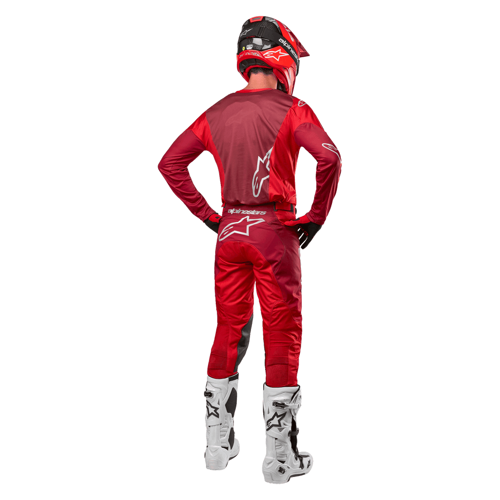 Pantalon et maillot assorti Alpinestars Racer Hoen 2024 en Mars Red Burgundy, vue arrière d'un pilote de motocross en tenue complète avec casque rouge et bottes blanches, illustrant la coupe athlétique et le marquage pour la course tout-terrain.