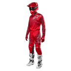 Pilote de motocross portant un équipement de course complet, pantalon et maillot Alpinestars Racer Hoen 2024 en Mars Red Burgundy, casque rouge, gants rouges et bottes blanches et noires, tenue coordonnée pour la course tout-terrain