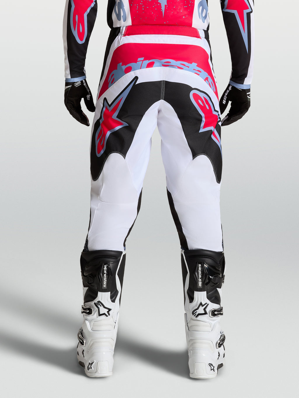 Alpinestars Fluid Drag, pantalon de motocross pour homme, blanc et noir avec des accents rouges, vue de dos, poly-tissu 600D durable, porté avec des bottes de moto blanches et noires, équipement de performance tout-terrain