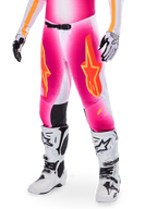 Alpinestars Supertech AFD MIG Limited Edition, pantalon de motocross, rose avec des logos d'étoiles orange et jaunes, porté avec des bottes de motocross blanches et des gants noirs et blancs, doté de panneaux intérieurs noirs aux genoux et d'une coupe athlétique, élément d'un ensemble d'équipement de course haute performance