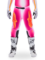 Pantalon Alpinestars Édition Limitée Supertech AFD MIG, pantalon de motocross, rose fluo et blanc avec des accents orange, avec de grands logos étoiles sur les cuisses, des panneaux perforés et des zones de préhension noires aux genoux, porté avec des bottes de motocross blanches et noires