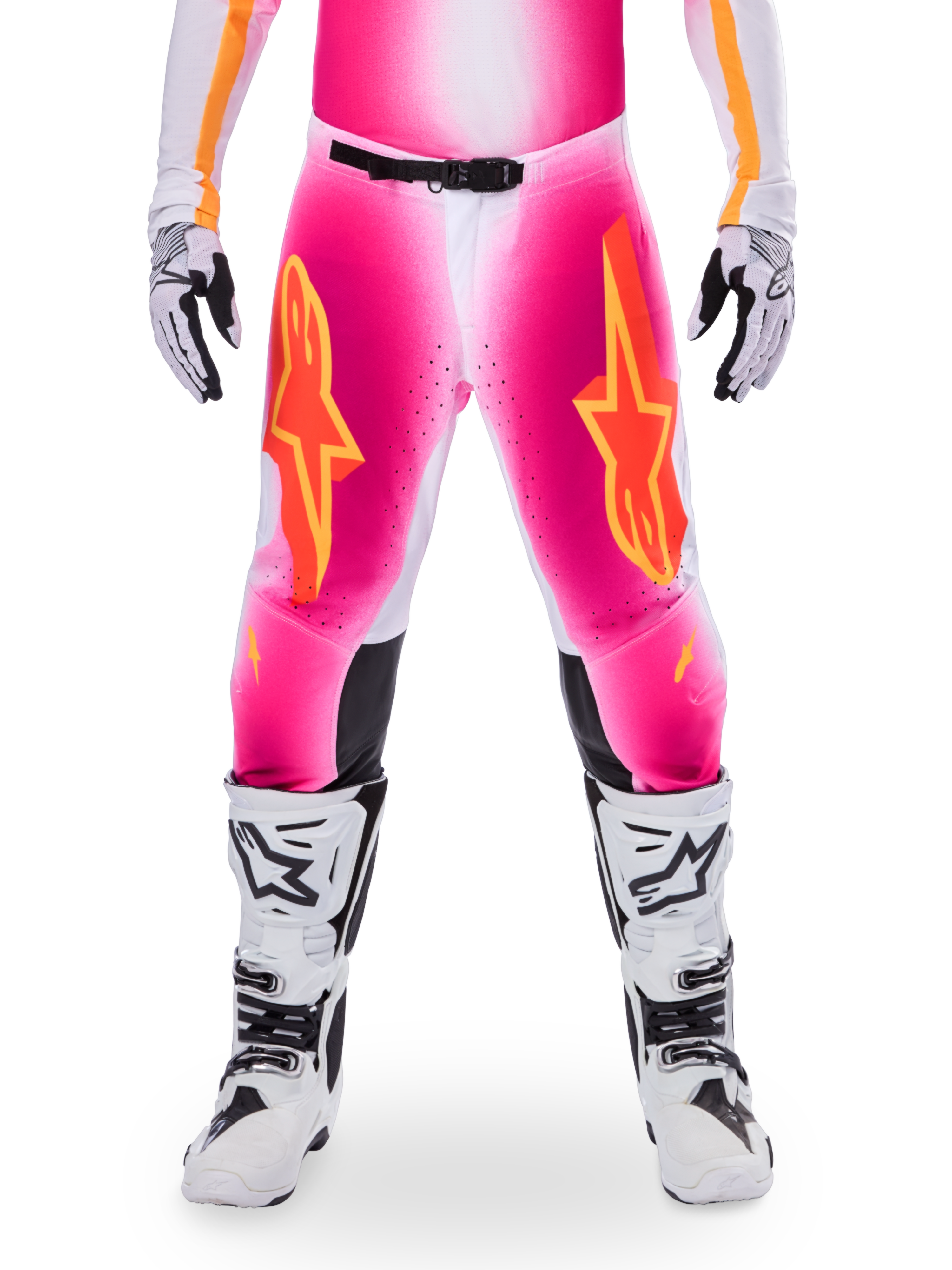 Pantalon Alpinestars Édition Limitée Supertech AFD MIG, pantalon de motocross, rose fluo et blanc avec des accents orange, avec de grands logos étoiles sur les cuisses, des panneaux perforés et des zones de préhension noires aux genoux, porté avec des bottes de motocross blanches et noires