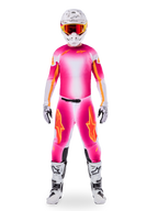 Pilote de motocross portant l'ensemble d'équipement Alpinestars Supertech AFD MIG en édition limitée, maillot et pantalon avec dégradé rose fluo et blanc et logos orange, casque blanc avec lunettes rouges, bottes et gants blancs et noirs, tenue de course professionnelle coordonnée.