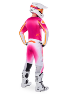 Pilote de motocross vu de dos portant la tenue Limited Edition Supertech AFD MIG, maillot rose avec accents orange, pantalon blanc avec dégradé rose et logo Alpinestars orange, casque blanc avec motifs roses et lunettes orange, bottes blanches et noires, équipement de course professionnel tout-terrain