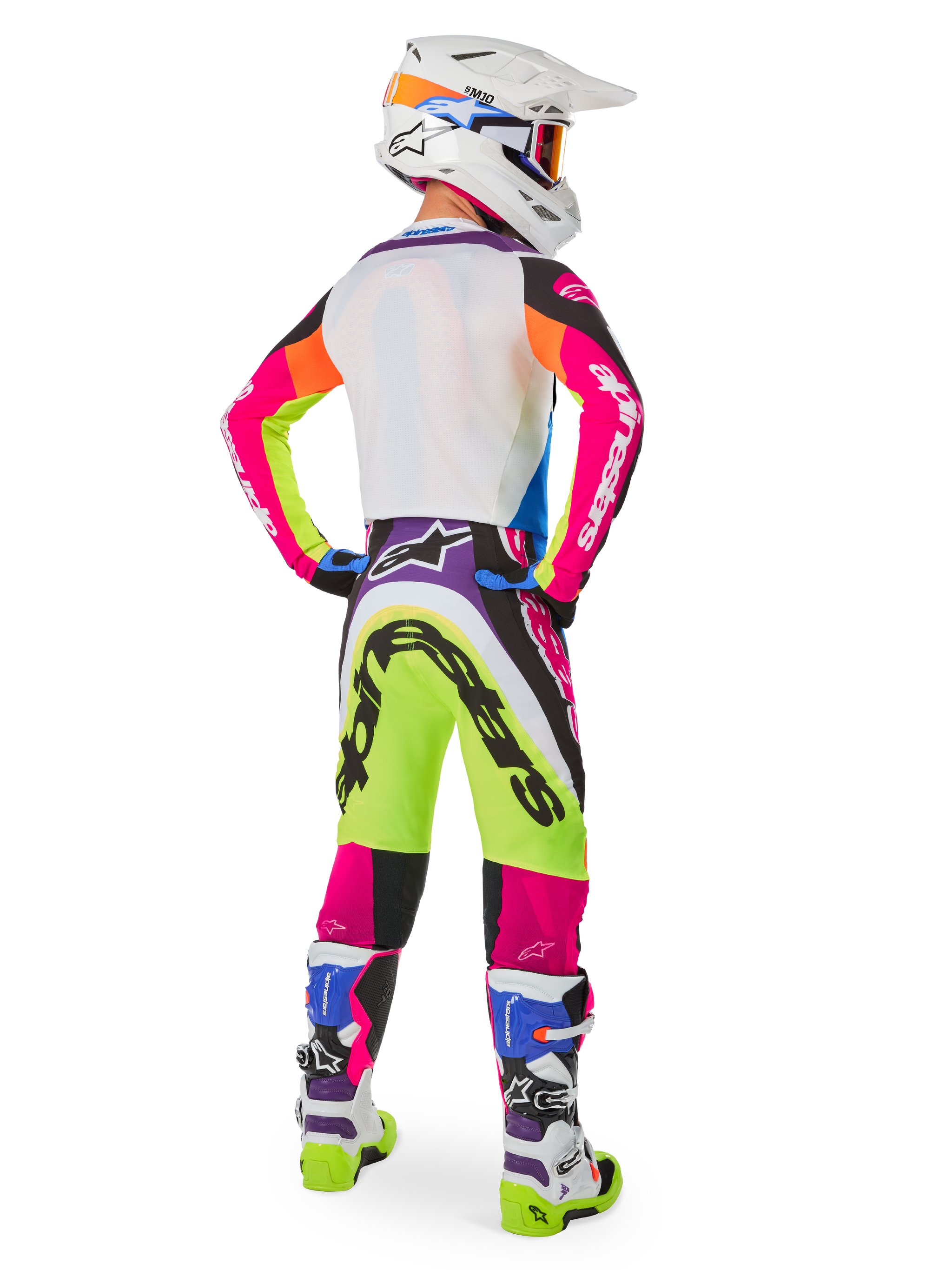 Pilote de motocross vu de dos portant l'équipement Alpinestars Limited Edition Supertech Hay, pantalon Supertech Hay multicolore aux graphismes jaune fluo, rose vif et violet, maillot assorti, casque blanc et bottes coordonnées blanches et bleues, tenue de course tout-terrain complète