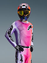 Motocross rider wearing the Alpinestars 2026 Racer Air Portl Jersey, Multicolor pink purple and orange gradient with white accents, matching colorful helmet and yellow goggles, black gloves, professional off-road racing gear