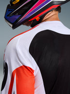 Alpinestars 2026 Racer Air Portl Jersey, maillot de motocross, multicolore avec panneaux blancs, noirs et rouges, gros plan sur la maille perforée au niveau de l'épaule et du dos pour la ventilation, porté avec un casque de motocross coloré