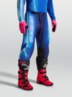 Pantalon Fluid Kepler Alpinestars, pantalon de motocross pour homme, bleu UCLA et bleu Blithe, poly-tissu 600D et jambes pré-courbées, porté avec des gants et des bottes de moto.