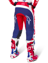 Alpinestars Techstar Fortitude Pants Édition Limitée, pantalon de motocross, rouge, blanc et bleu, vue arrière porté avec des bottes rouges et blanches assorties, arborant des logos d'étoiles blanches sur les cuisses, conception multi-panneaux durable pour la course tout-terrain professionnelle
