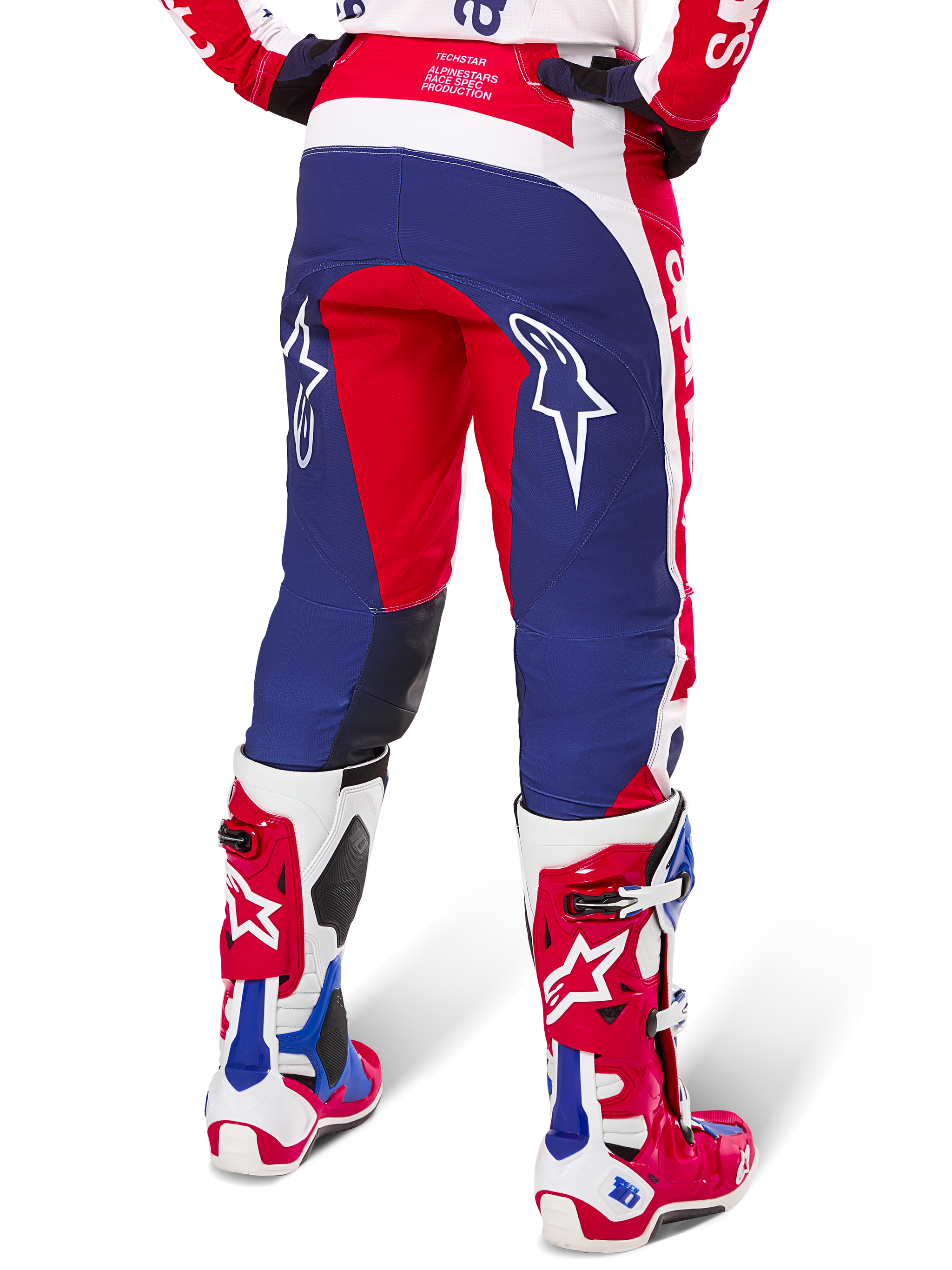 Alpinestars Techstar Fortitude Pants Édition Limitée, pantalon de motocross, rouge, blanc et bleu, vue arrière porté avec des bottes rouges et blanches assorties, arborant des logos d'étoiles blanches sur les cuisses, conception multi-panneaux durable pour la course tout-terrain professionnelle