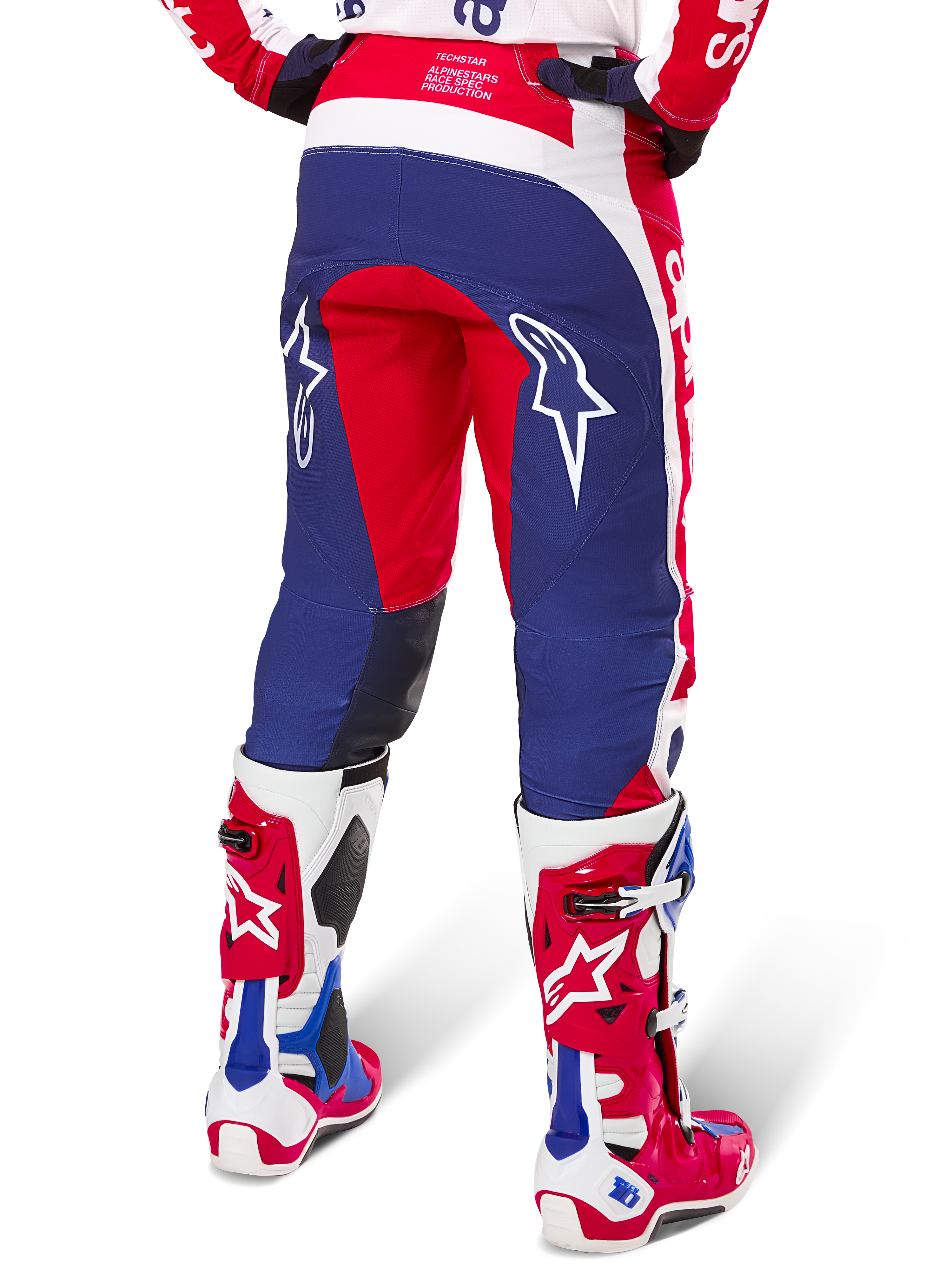Alpinestars Techstar Fortitude Pants Édition Limitée, pantalon de motocross, rouge, blanc et bleu, vue arrière porté avec des bottes rouges et blanches assorties, arborant des logos d'étoiles blanches sur les cuisses, conception multi-panneaux durable pour la course tout-terrain professionnelle
