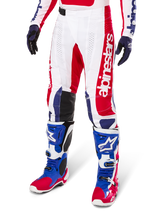 Alpinestars Limited Edition Techstar Fortitude Pants, pantalon de motocross, rouge vif, blanc et bleu, porté avec des bottes et gants tout-terrain assortis, logo vertical sur la jambe, panneaux perforés respirants et sections renforcées noires aux genoux, coupe de course athlétique
