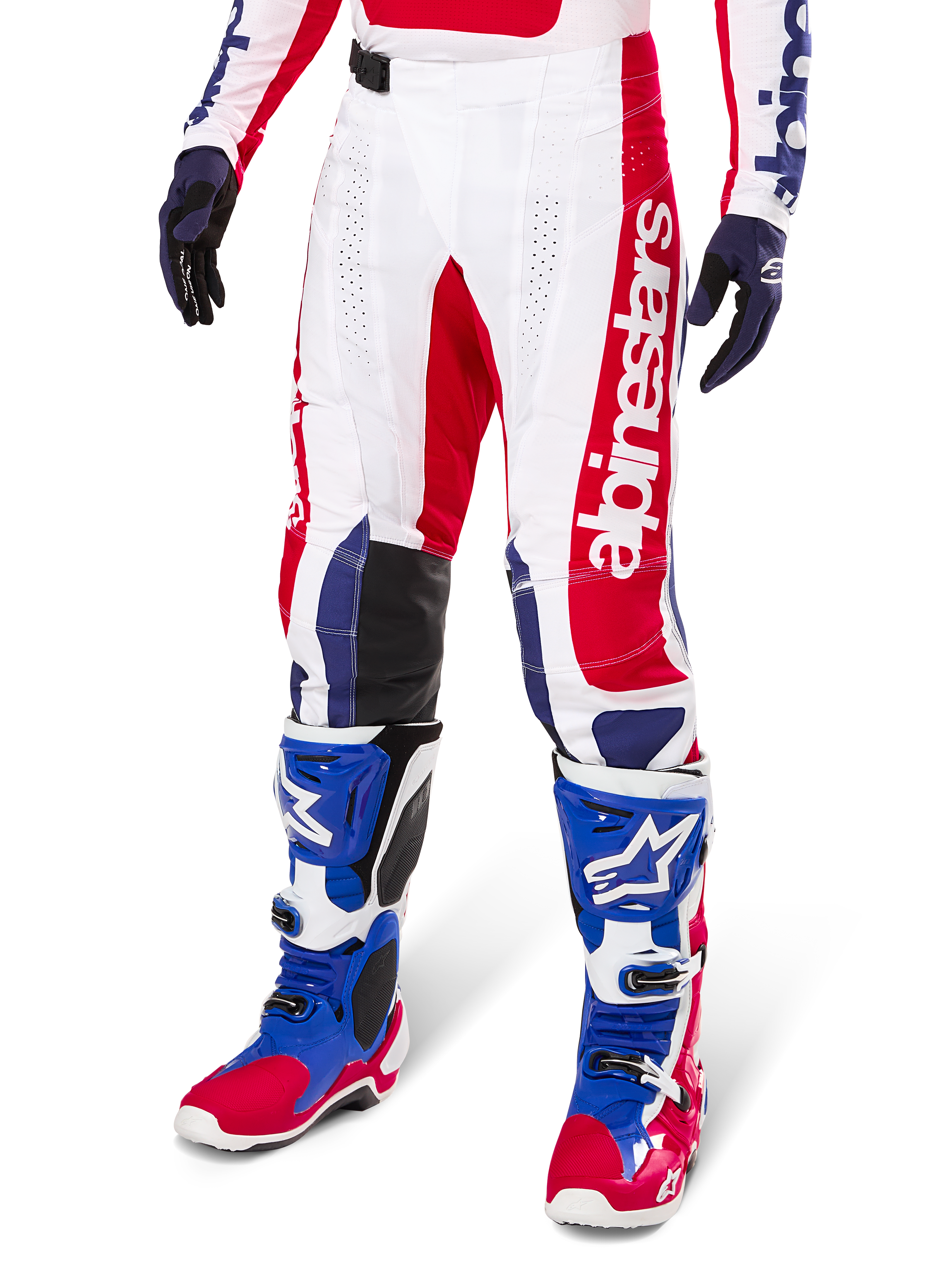 Alpinestars Limited Edition Techstar Fortitude Pants, pantalon de motocross, rouge vif, blanc et bleu, porté avec des bottes et gants tout-terrain assortis, logo vertical sur la jambe, panneaux perforés respirants et sections renforcées noires aux genoux, coupe de course athlétique