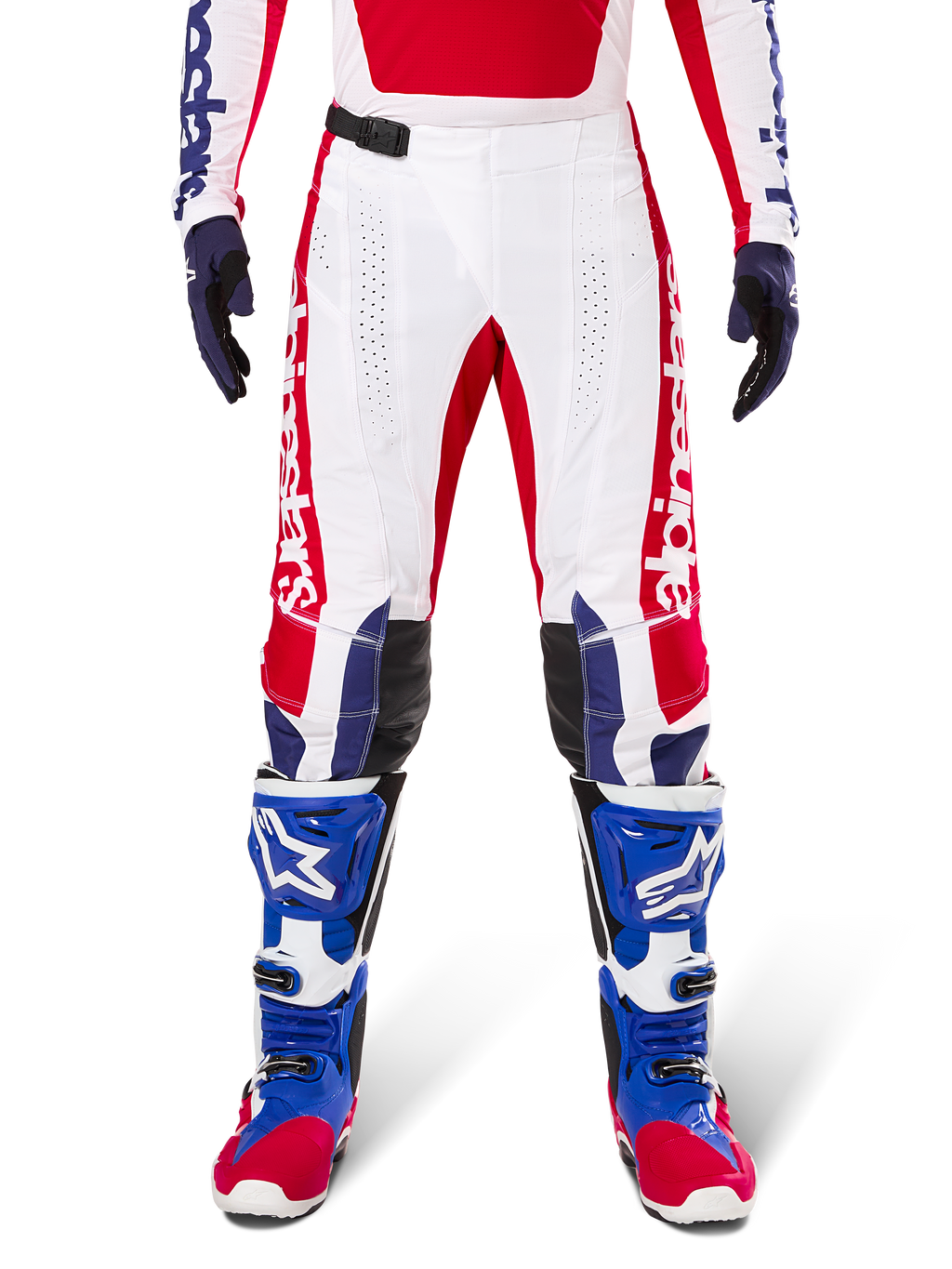 Alpinestars Limited Edition Techstar Fortitude Pants, pantalon de motocross, rouge vif, blanc et bleu, porté avec l'équipement assorti incluant des bottes de protection et des gants bleus, présentant un châssis blanc avec des graphismes rouges, des empiècements aux genoux en cuir noir et des perforations découpées au laser, tenue de course tout-terrain professionnelle