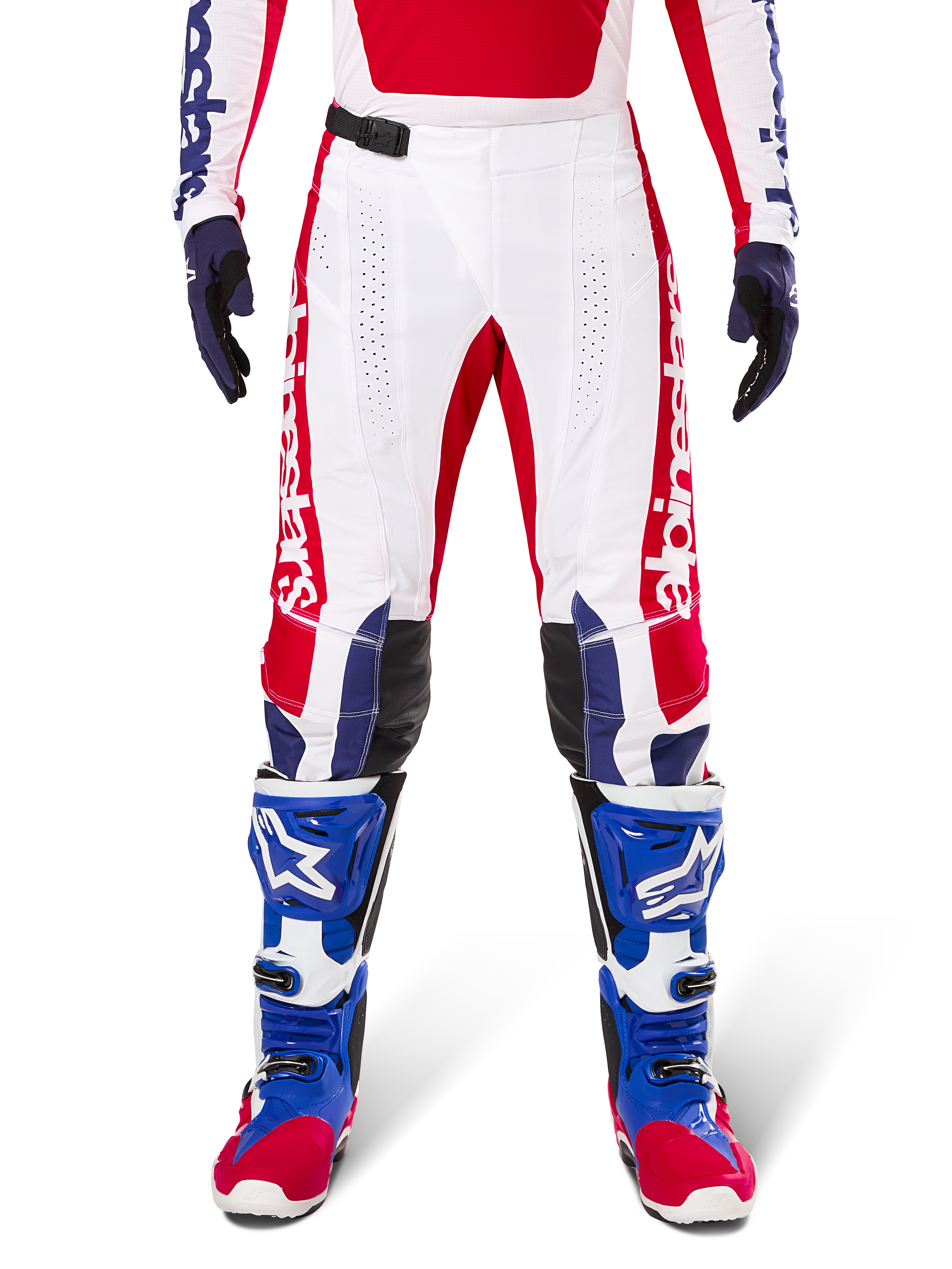 Alpinestars Limited Edition Techstar Fortitude Pants, pantalon de motocross, rouge vif, blanc et bleu, porté avec l'équipement assorti incluant des bottes de protection et des gants bleus, présentant un châssis blanc avec des graphismes rouges, des empiècements aux genoux en cuir noir et des perforations découpées au laser, tenue de course tout-terrain professionnelle