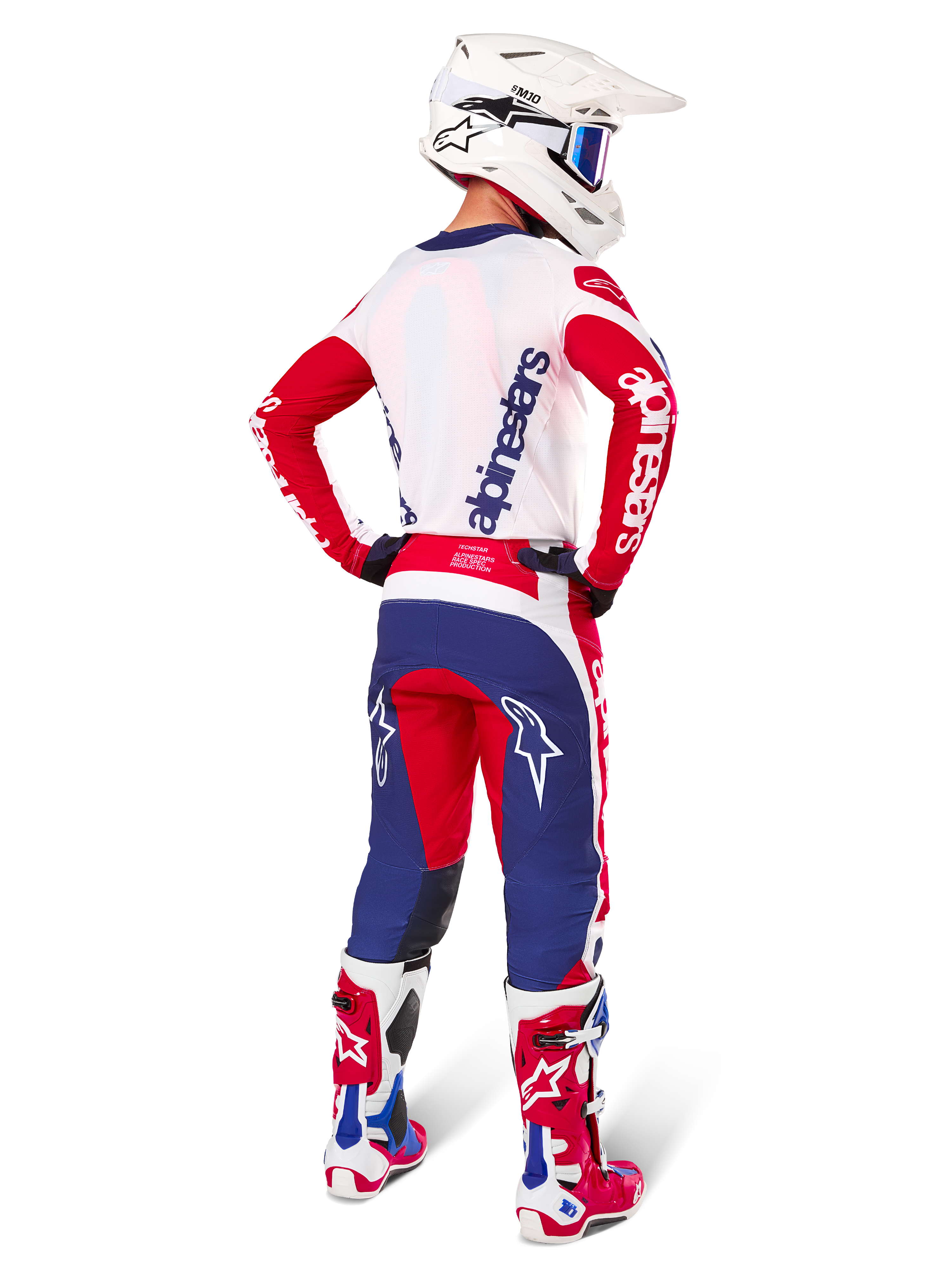 Alpinestars Techstar Fortitude Édition Limitée, pantalon de motocross, rouge vif, blanc et bleu, vu de dos sur un pilote avec maillot, bottes et casque assortis, mettant en avant la coupe athlétique et l'emplacement du logo.