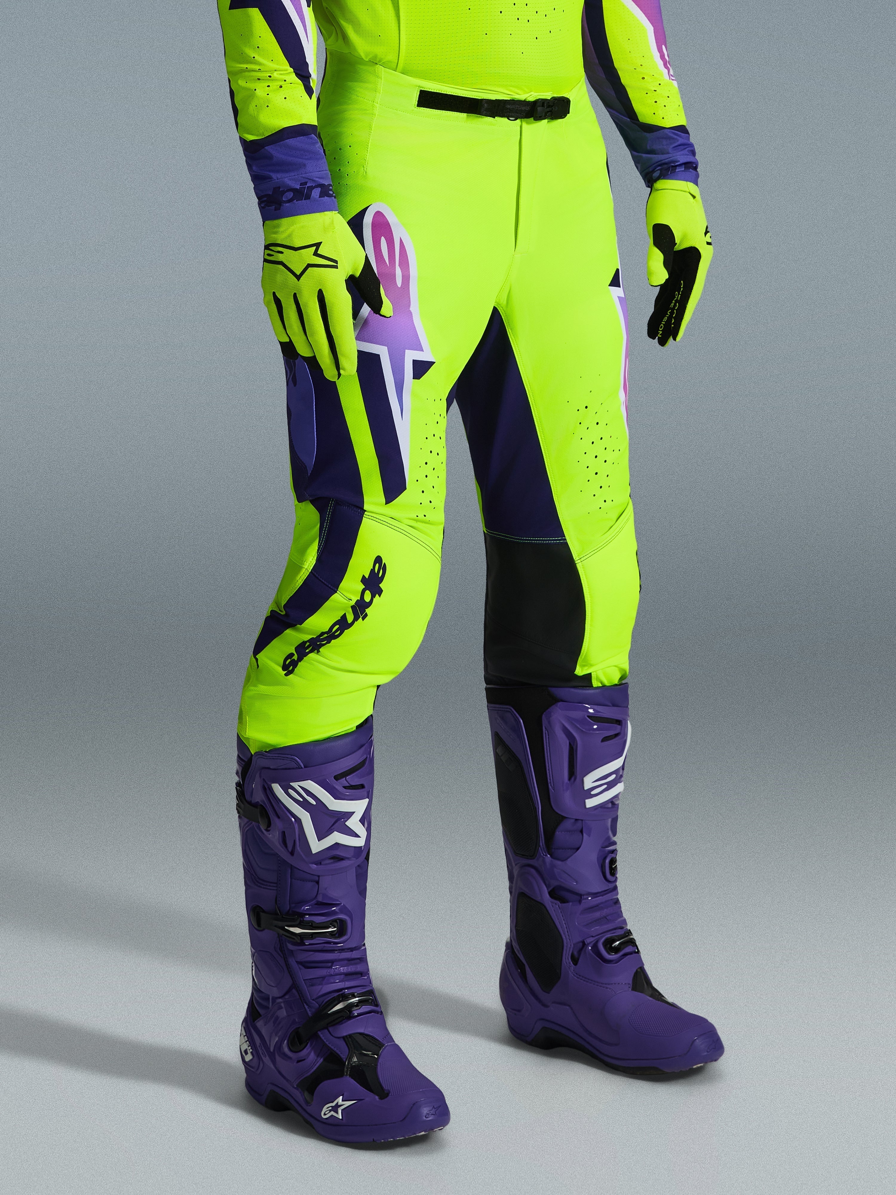 Pantalon Alpinestars Supertech Vista 2026, pantalon de motocross, jaune néon éclatant, violet et noir, porté avec des bottes violettes et des gants jaunes assortis, arborant un logo imposant sur la cuisse et une coupe athlétique haute performance.
