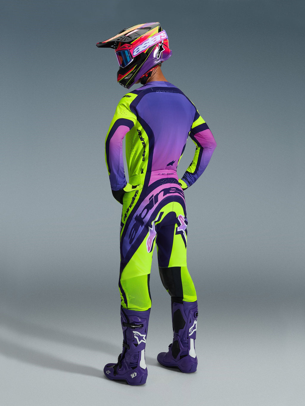 Alpinestars 2026 Supertech Vista Pants, pantalon de motocross, jaune, violet et noir avec dégradés roses, vue arrière du pilote avec maillot assorti, bottes de course violettes et casque multicolore, équipement tout-terrain haute performance