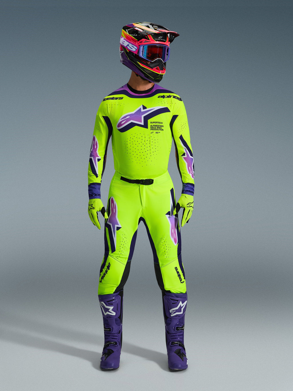 Pilote de motocross portant le maillot Alpinestars 2026 Supertech Vista jaune vif avec des accents violets et noirs, pantalon jaune et violet assorti, bottes violettes, casque et gants coordonnés, ensemble complet d'équipement de course professionnel
