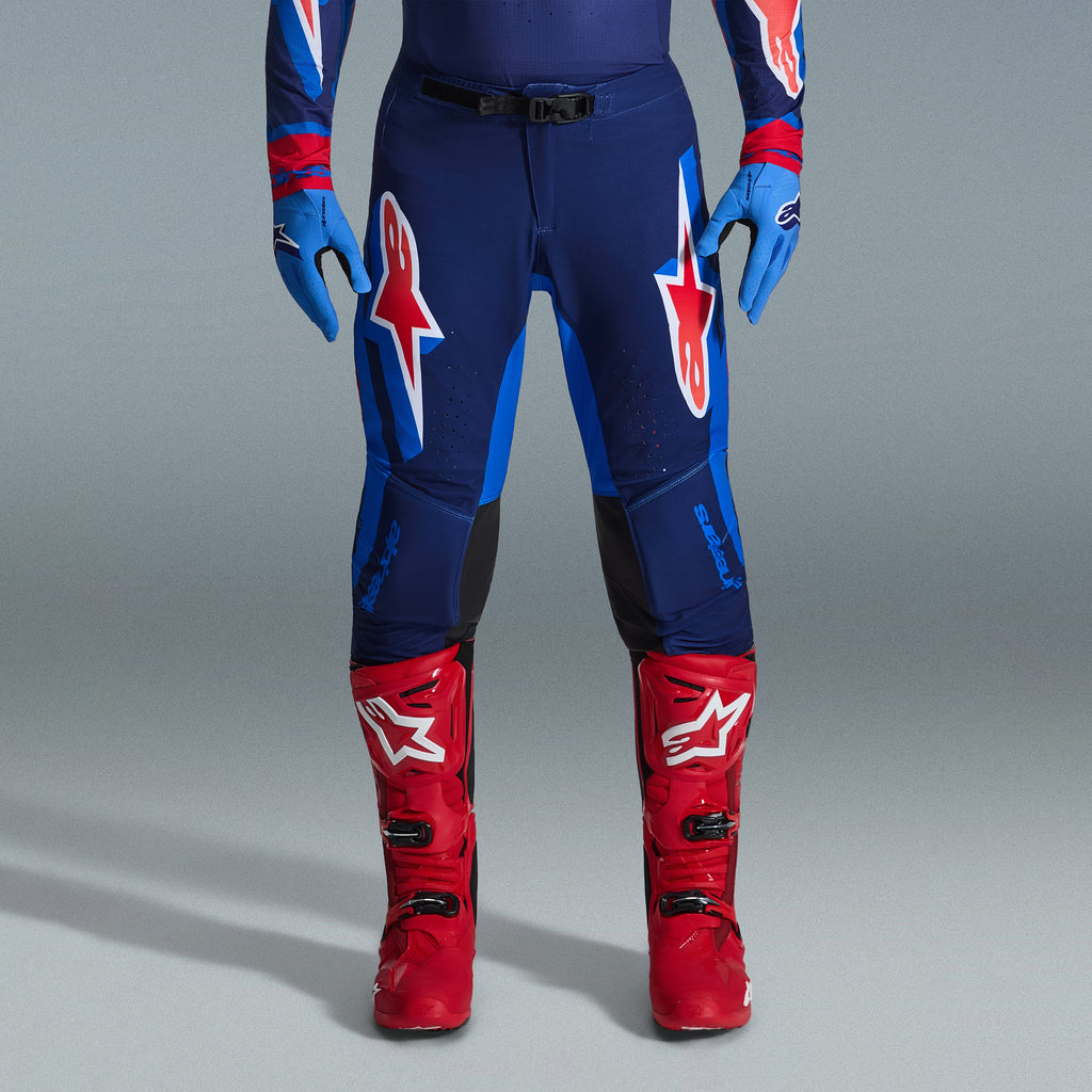 Ensemble d'équipement Alpinestars Supertech Vista 2026, pantalon de motocross bleu marine et bleu vif avec logos rouges et blancs, associé à des gants bleu clair et des bottes de motocross rouge vif, tenue de course professionnelle.